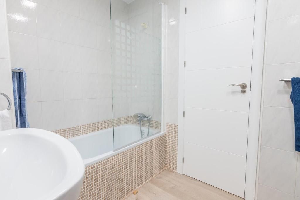 Baño blanco con bañera, mampara de cristal y puerta blanca.