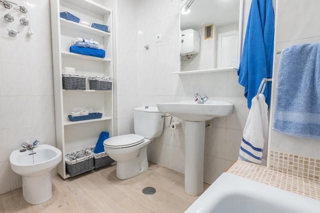 Un baño blanco con toallas y detalles azules; incluye inodoro, lavabo, bidé y estanterías.