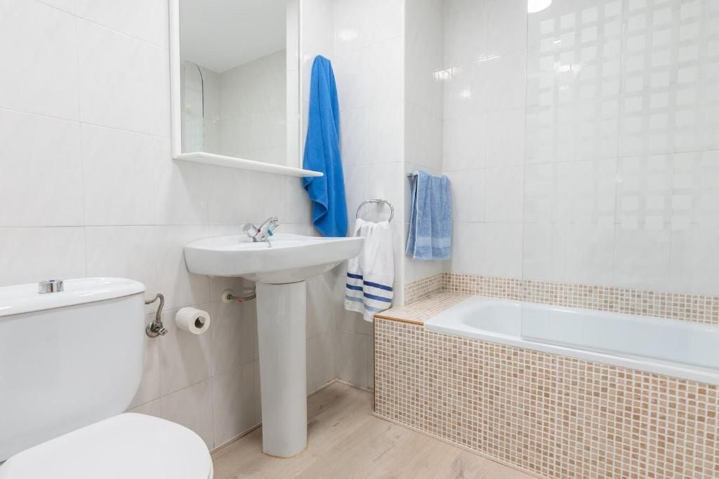 Un baño pequeño y blanco con inodoro, lavabo, espejo y bañera. Toallas azules colgadas en la habitación.