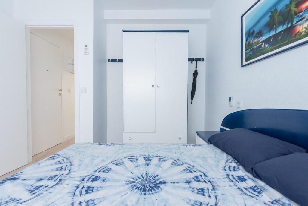 Dormitorio con paredes blancas, armario y cama con ropa de cama estampada en color azul.