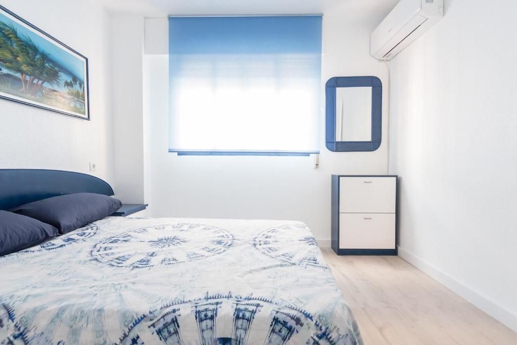 Dormitorio con paredes blancas, detalles en azul, cama con ropa de cama estampada en azul y una ventana con persiana azul.