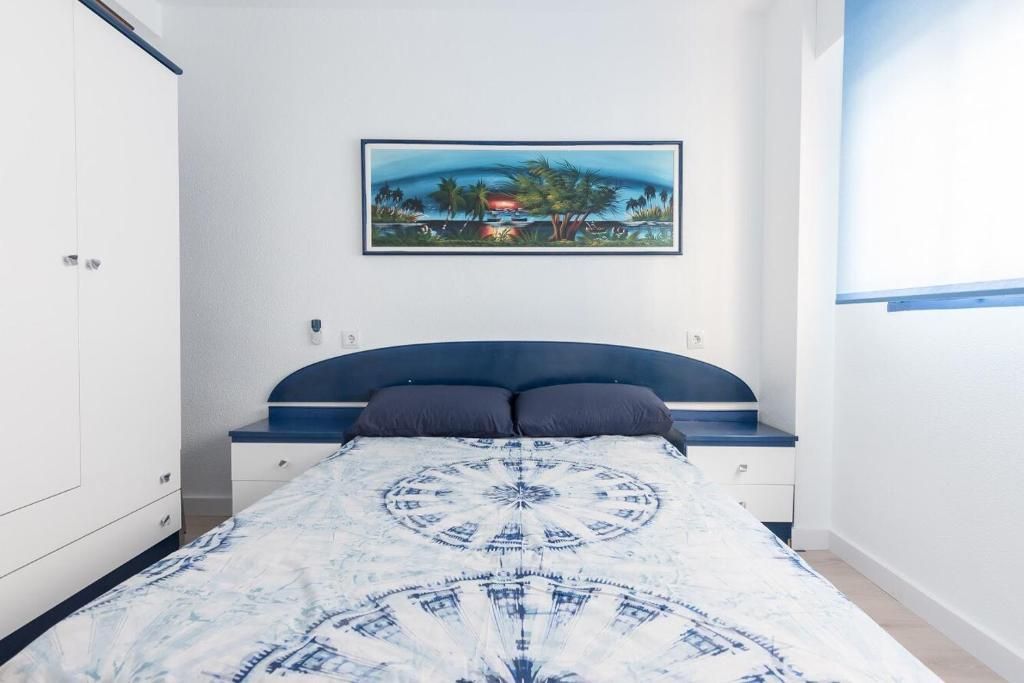 Dormitorio con cama, cabecero azul y blanco, mesitas de noche, cuadro y armario.