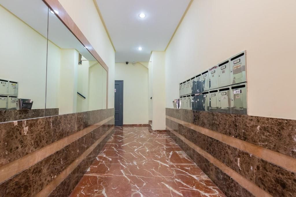 Pasillo con detalles de mármol, buzones y un espejo grande. Paredes beige y suelo de baldosas marrón rojizas.