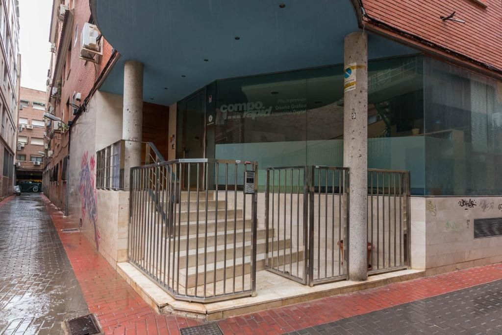 Entrada a edificio con escalones, paredes de cristal y portón metálico, con callejón lateral.