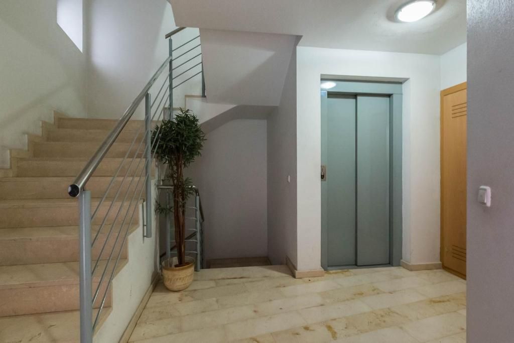 Escalera con barandilla de acero inoxidable y ascensor en la entrada de un edificio. Cerca hay una maceta.