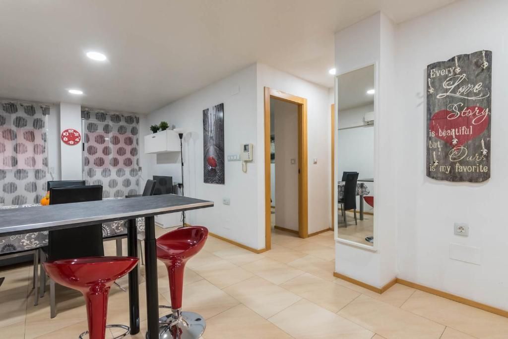 Sala de estar con taburetes rojos, una mesa negra, obras de arte y una puerta abierta.