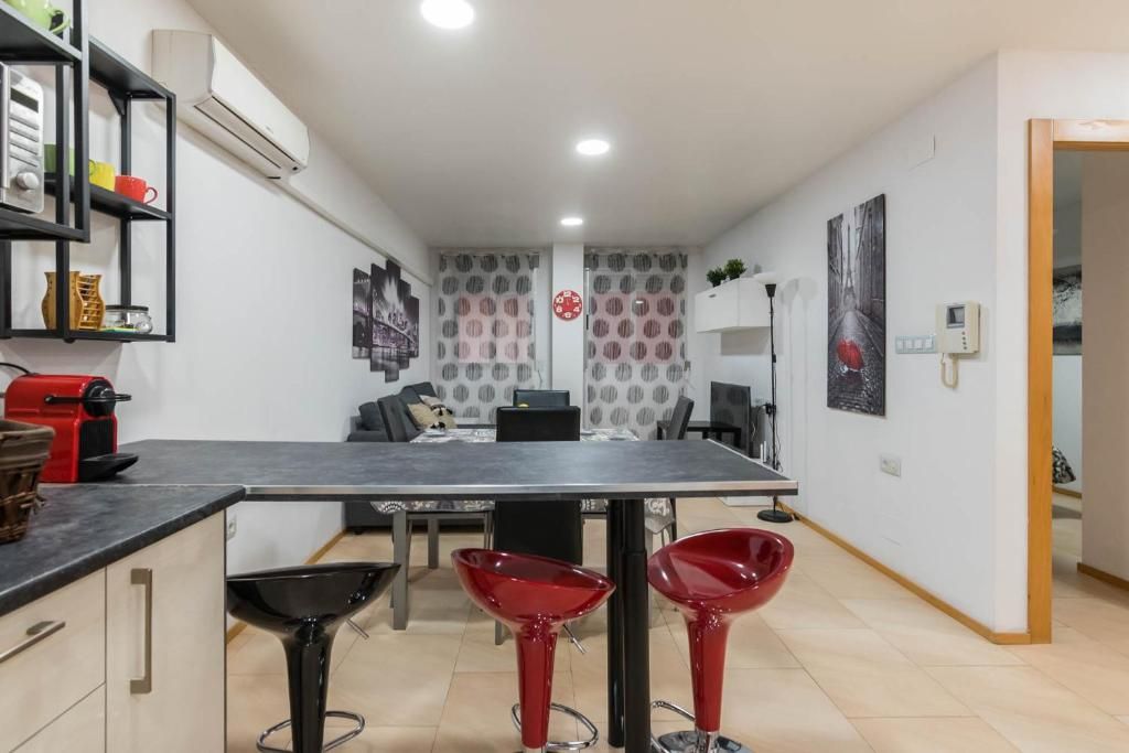 Cocina con encimera negra, taburetes de bar rojos y negros y mesa de comedor.