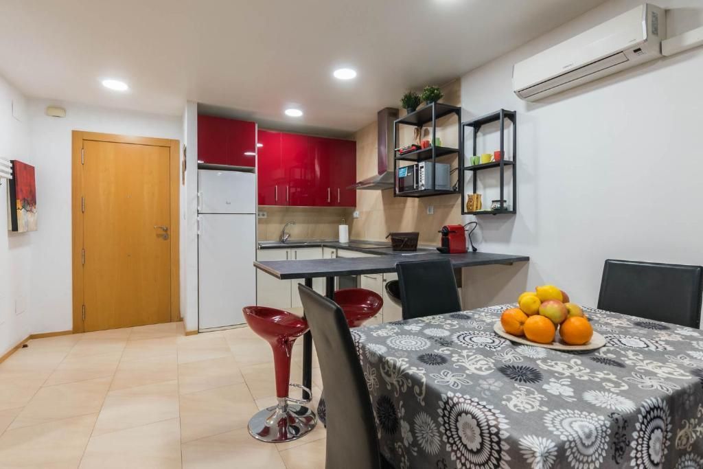 Cocina-comedor interior. Armarios rojos, taburetes y una mesa con naranjas. Puerta a la izquierda.