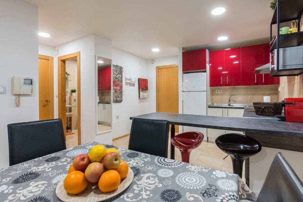 Cocina y comedor con gabinetes rojos, encimera gris y un frutero sobre la mesa.