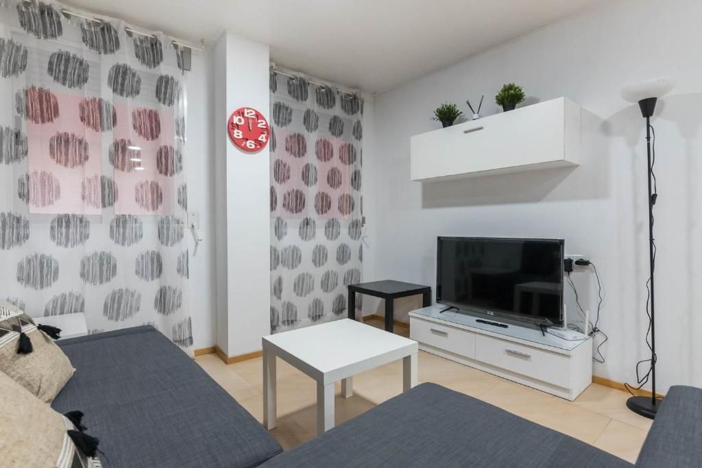 Sala de estar con sofá gris, muebles blancos, TV y cortinas de lunares.