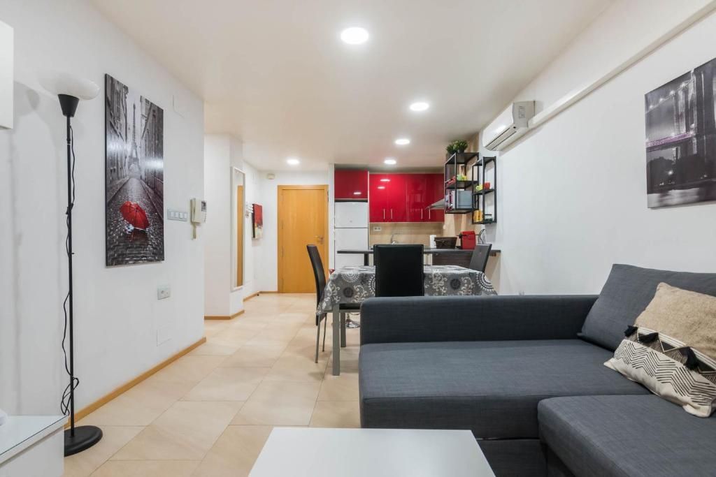 Sala de estar con un sofá seccional gris, cocina con gabinetes rojos, arte en paredes blancas y una puerta de madera.