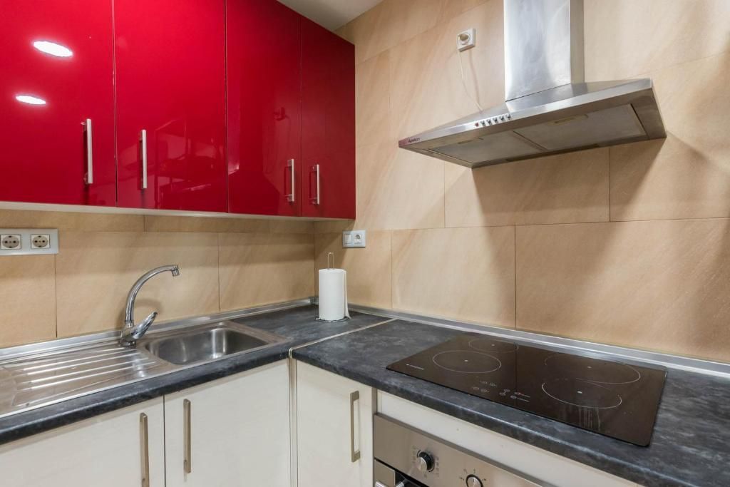 Gabinetes de cocina rojos sobre un fregadero, una estufa y un horno con gabinetes blancos debajo.