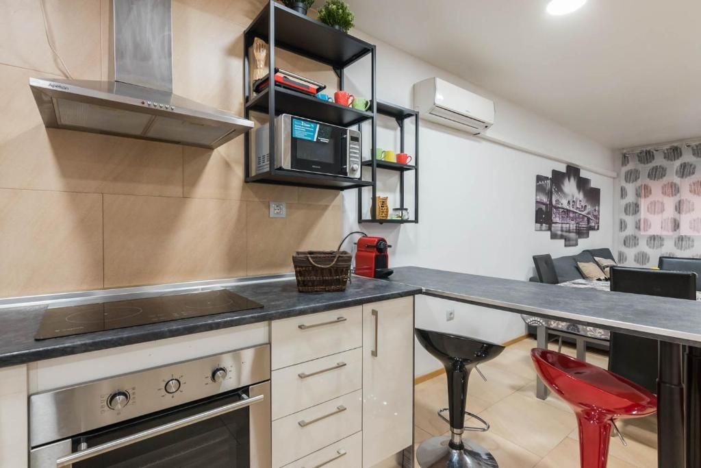 Cocina moderna con encimeras negras, electrodomésticos de acero inoxidable y un taburete rojo.