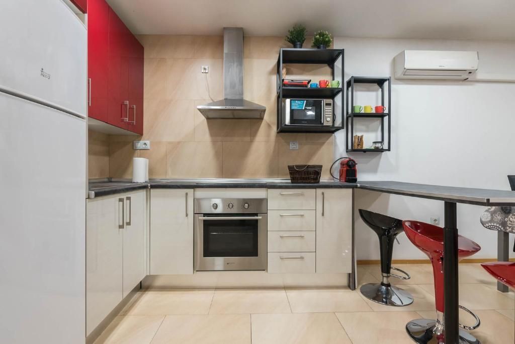 Cocina con gabinetes blancos y rojos, electrodomésticos de acero inoxidable y una barra con taburetes rojos.