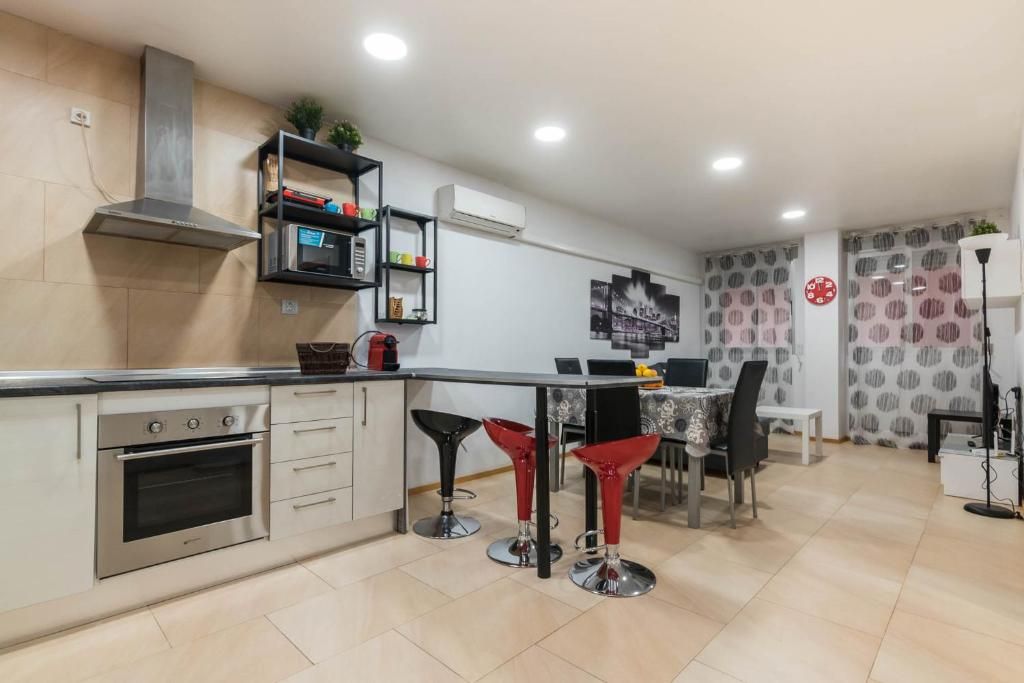 Cocina con electrodomésticos de acero inoxidable, taburetes de bar negros y área de comedor con cortinas estampadas redondas.