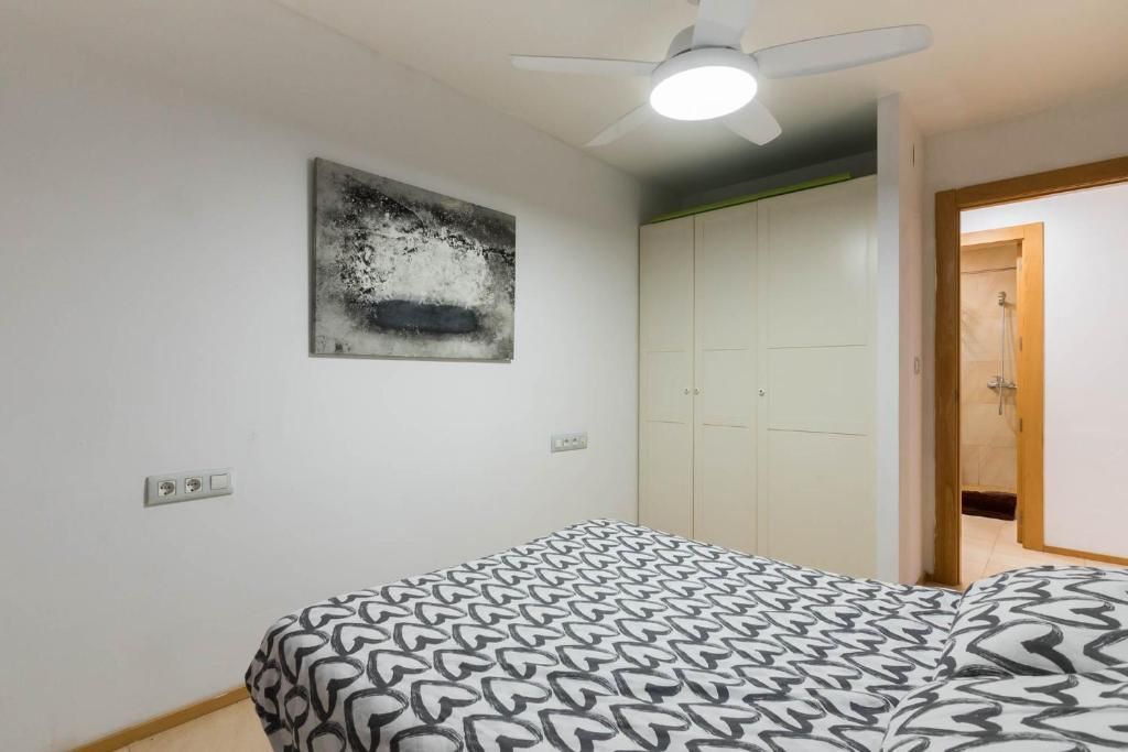 Dormitorio con cama, paredes blancas, arte abstracto, armario y puerta a otra habitación.