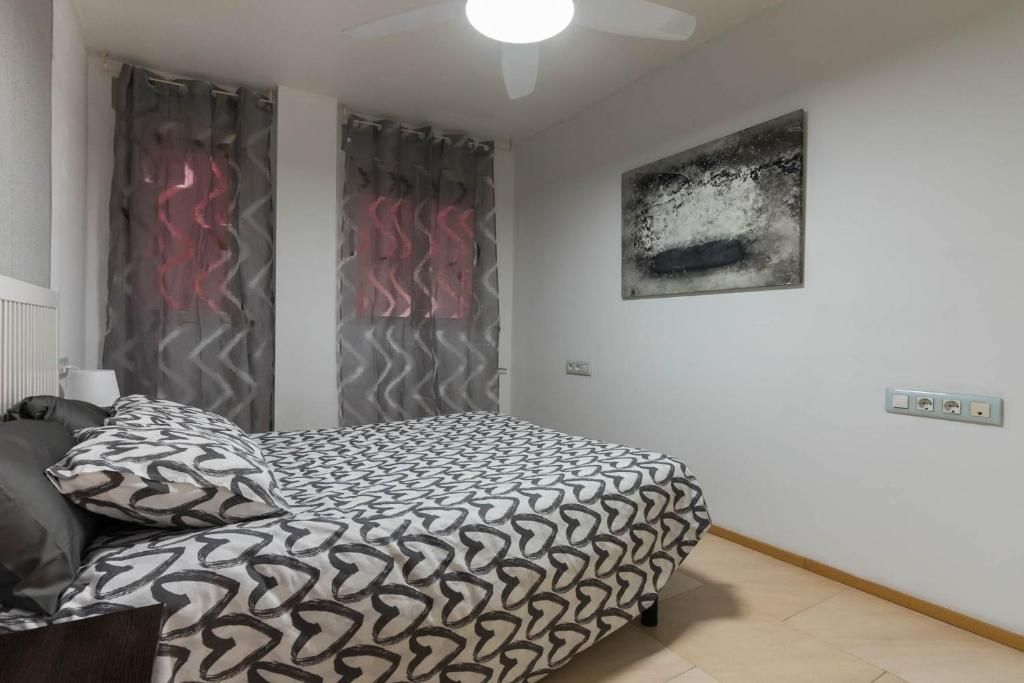 Dormitorio con cama, funda estampada, cortinas grises, arte y ventilador de techo.