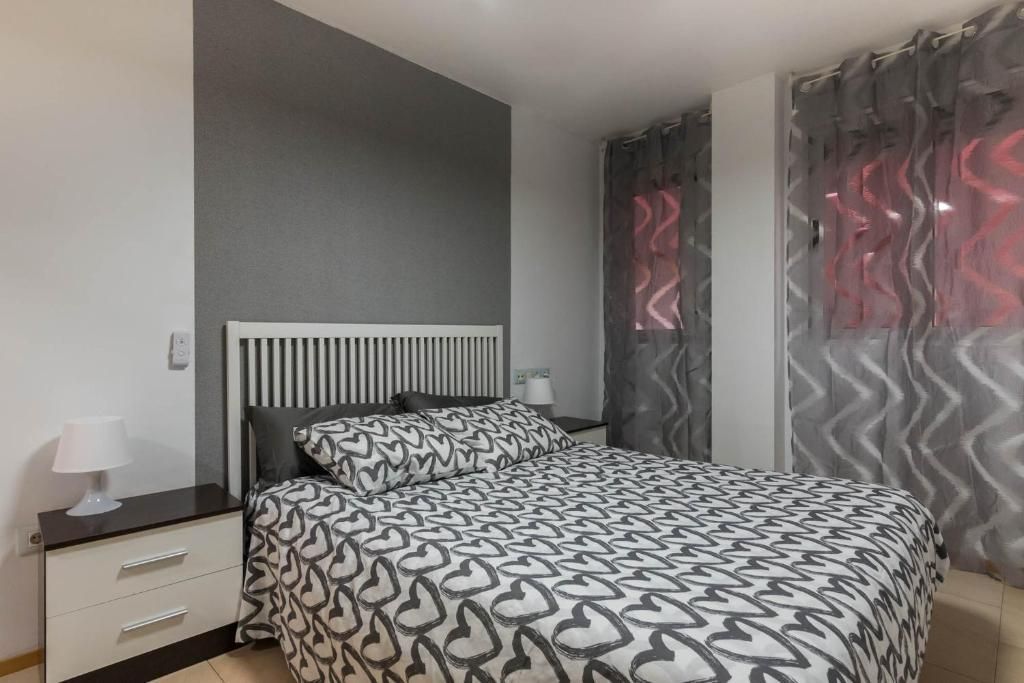 Dormitorio con una pared con acento gris, ropa de cama estampada en blanco y gris y cortinas transparentes.