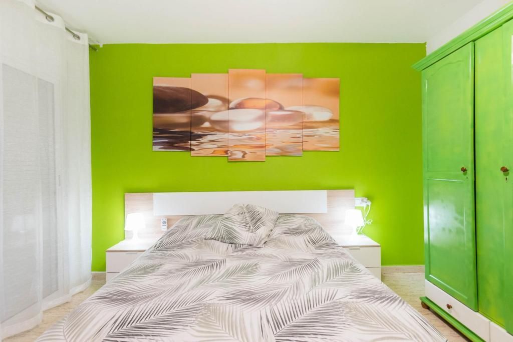 Dormitorio con una pared con acento verde lima, cama blanca, armario verde y obras de arte.