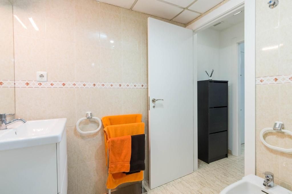 Interior de baño con lavabo blanco, toallas naranjas y negras en un estante y una puerta a otra habitación.