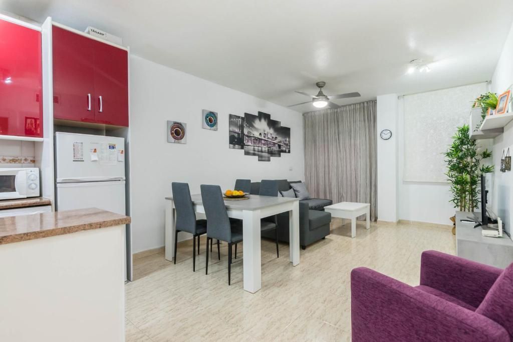 Sala de estar con cocina, comedor y asientos. Armarios rojos, sofá gris, sillones morados y obras de arte.