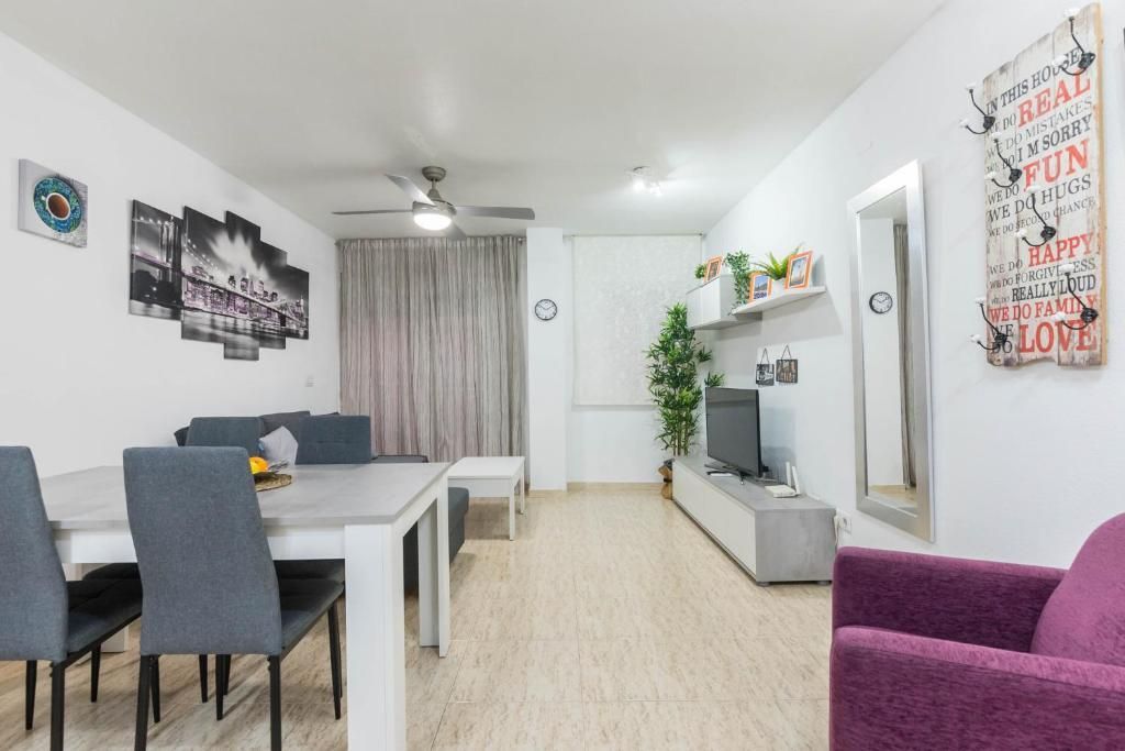 Sala de estar con paredes blancas, sofá gris, mesa de comedor y decoraciones.