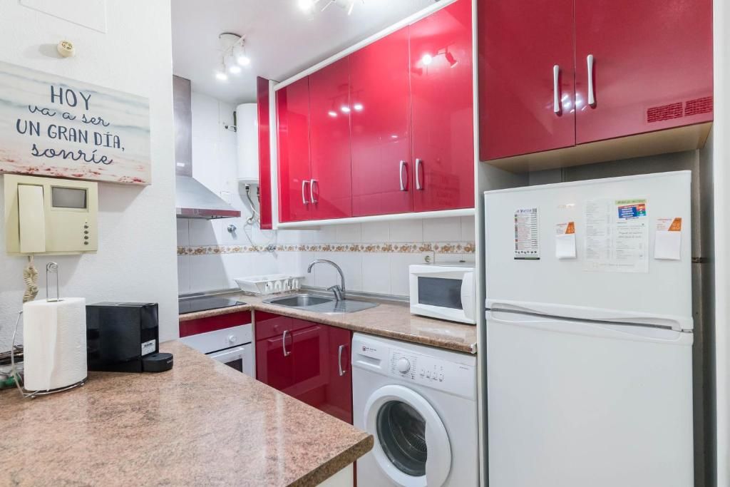 Cocina con gabinetes rojos, electrodomésticos blancos y encimera de granito.