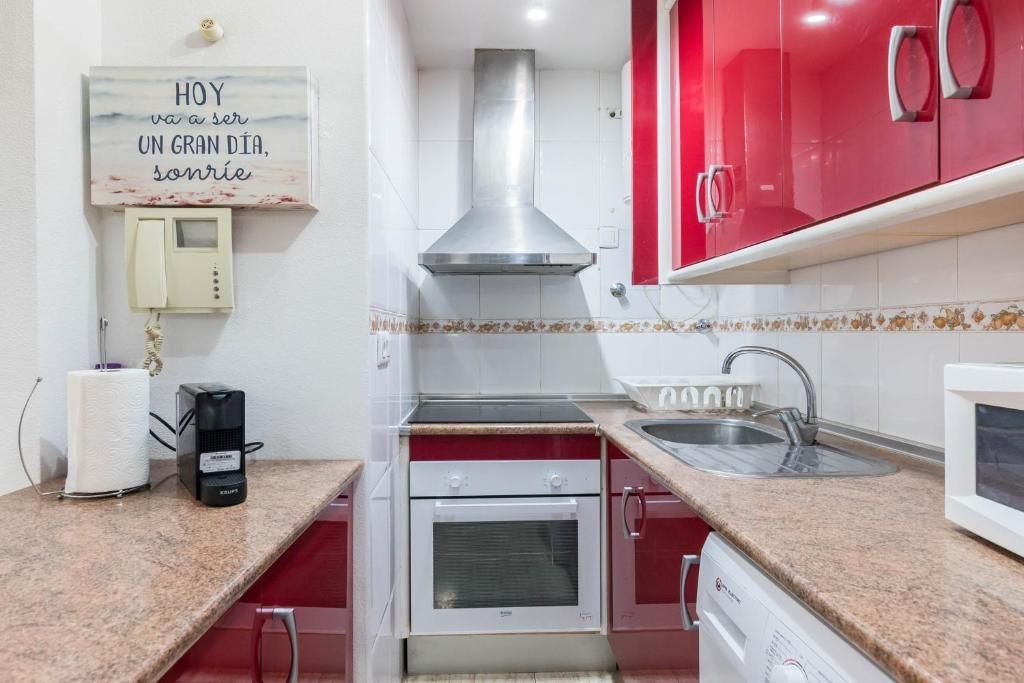 Cocina pequeña con gabinetes rojos, electrodomésticos de acero inoxidable y encimeras de color beige.