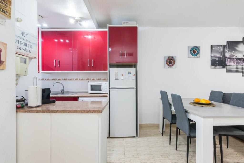 Cocina con gabinetes rojos, refrigerador blanco y una mesa de comedor con sillas.