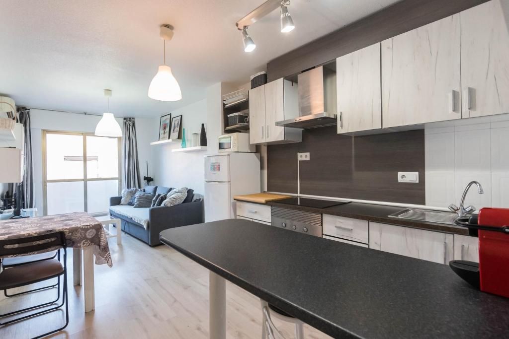 Espacio habitable de planta abierta con cocina y sala de estar, con pisos de madera clara y gabinetes blancos.