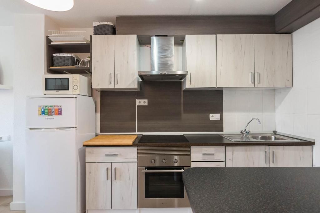 Una cocina pequeña y moderna con gabinetes de madera clara, electrodomésticos de acero inoxidable y un refrigerador blanco.