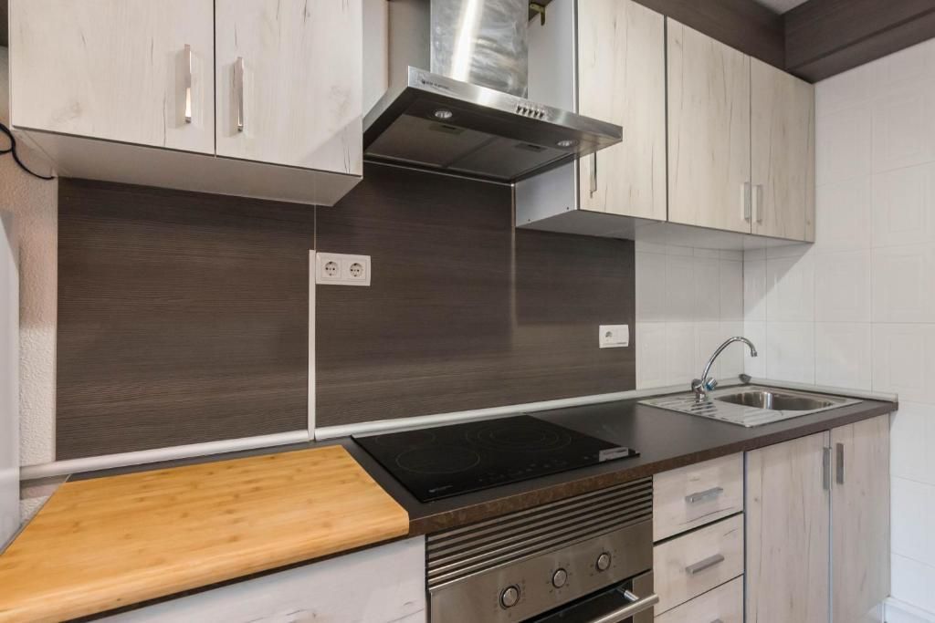 Cocina con gabinetes de madera clara, encimera oscura, electrodomésticos de acero inoxidable y protector contra salpicaduras.