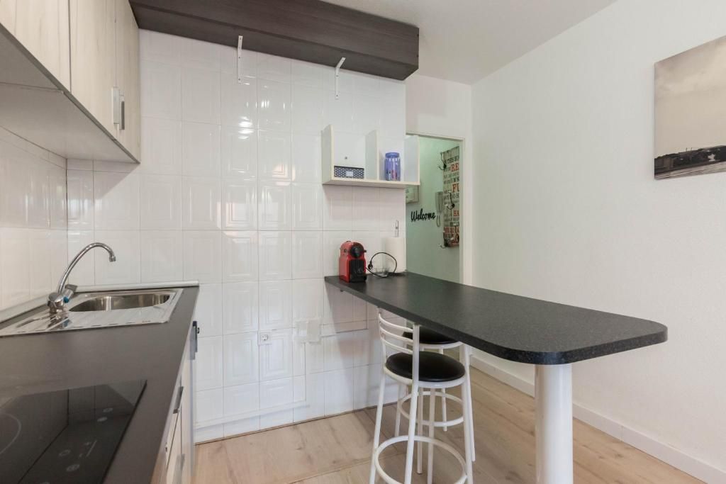 Cocina pequeña con salpicadero de azulejos blancos, fregadero y encimera negra con mesa de bar y taburete.