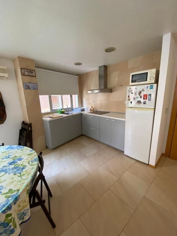 Cocina con gabinetes grises, refrigerador blanco y una mesa redonda con mantel floral.
