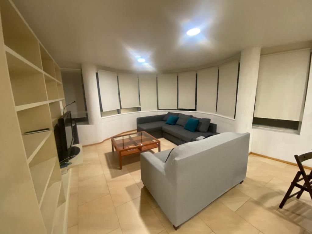 Sala de estar con sofá gris, mesa de café y estanterías empotradas; pared curva con cortinas.