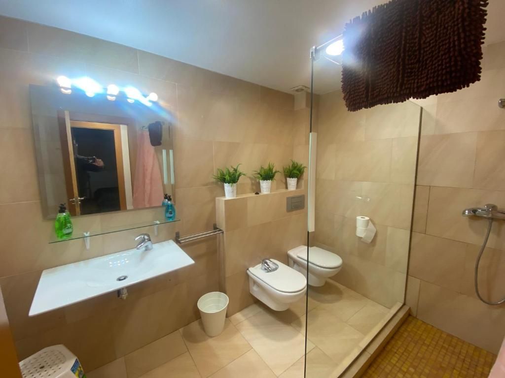 Baño con paredes de azulejos color canela, lavabo e inodoro blancos y ducha de cristal.