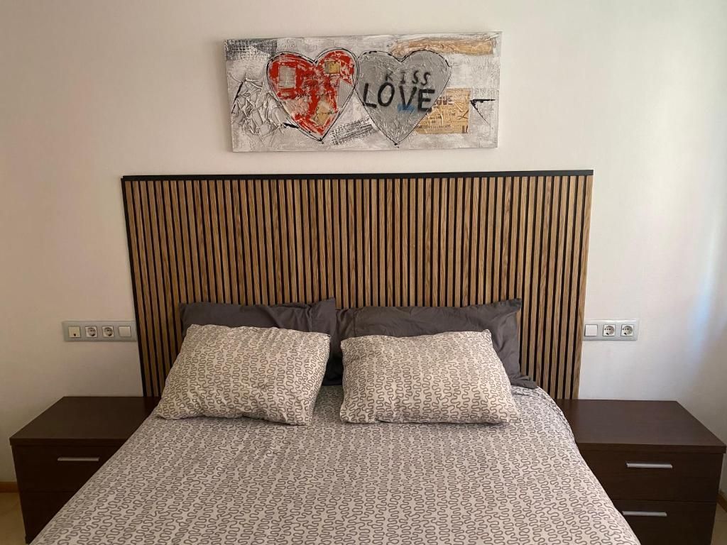 Dormitorio con cabecero de madera, dos almohadas y obra de arte de corazones que dicen 