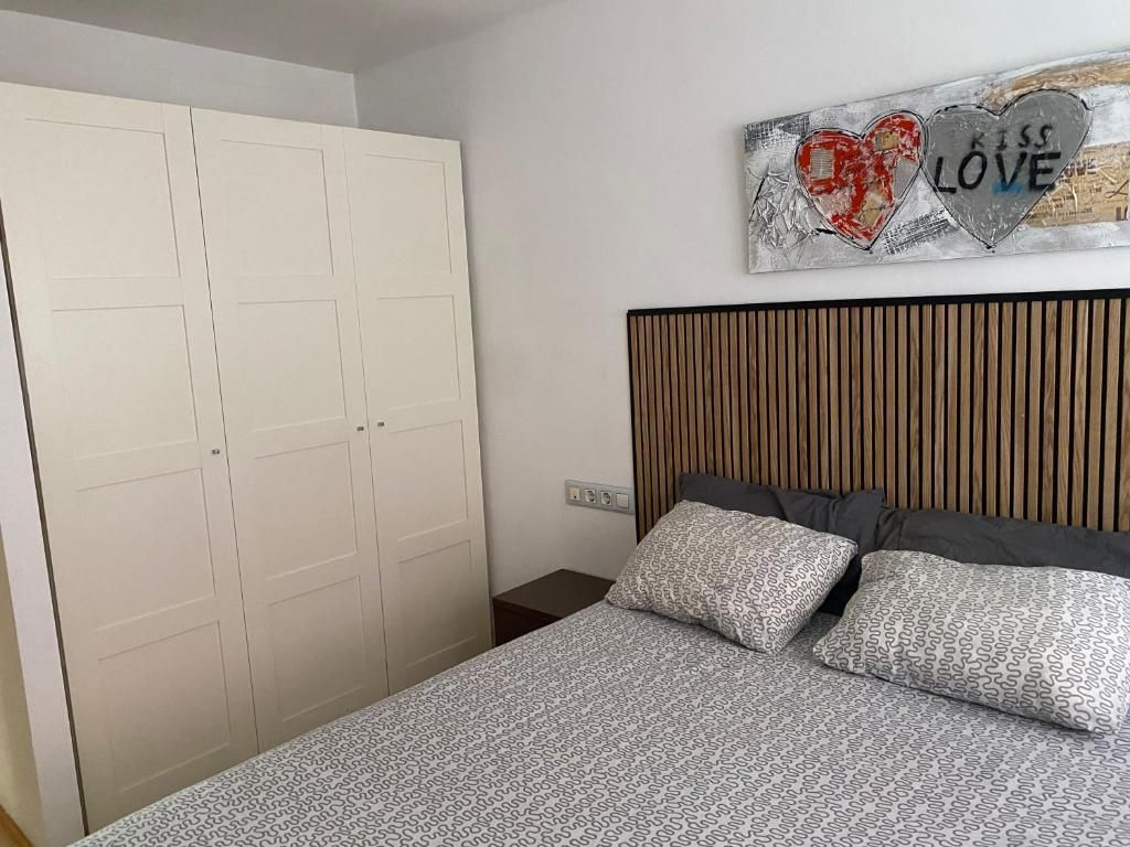 Dormitorio con cama, cabecero, armario y obras de arte. Ropa de cama gris y paredes blancas.