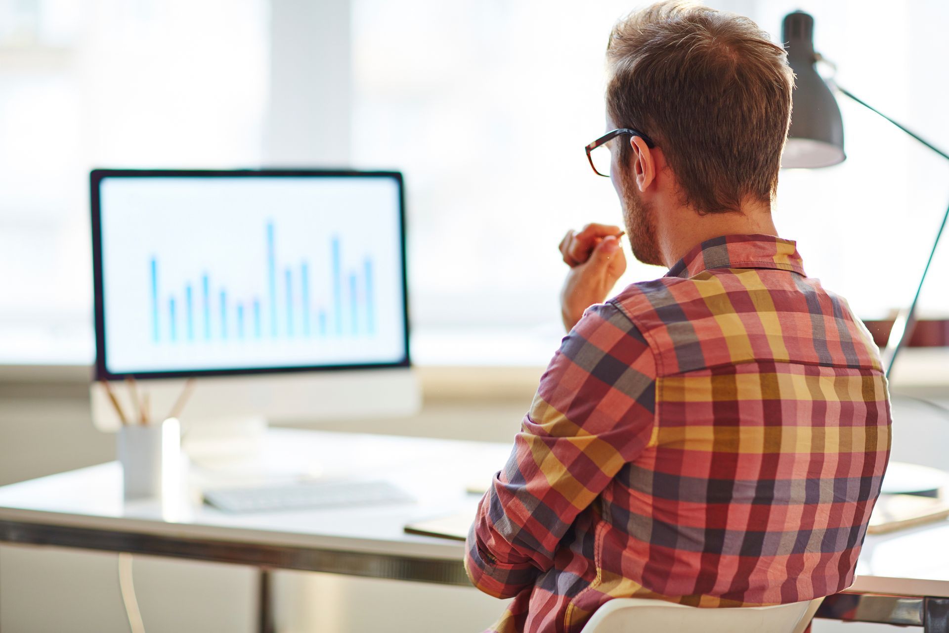 Un hombre con camisa a cuadros mira la pantalla de una computadora con un gráfico, sentado en el escritorio.