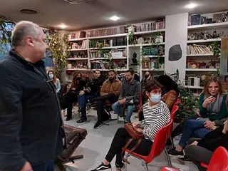 Un hombre está de pie frente a un grupo de personas sentadas en sillas en una habitación.
