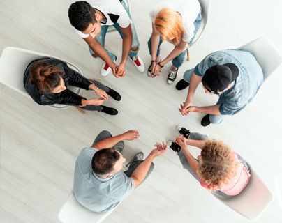 Un grupo de personas están sentadas en círculo tomadas de la mano.