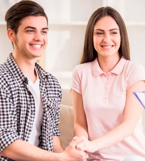 Un hombre y una mujer están sentados en un sofá tomados de la mano y sonriendo.