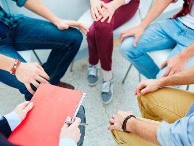 Un grupo de personas están sentadas en círculo tomadas de la mano.