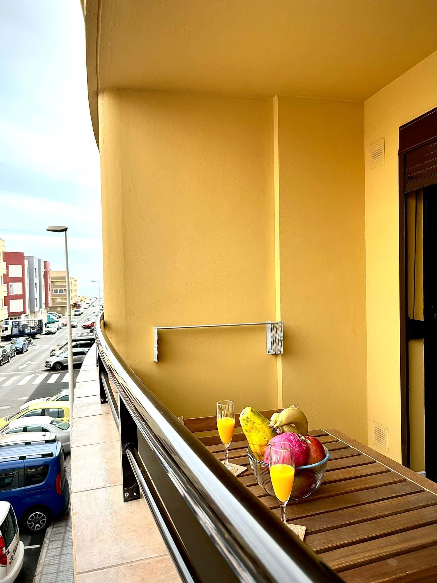 Balcón a la calle, con mesa de madera con frutas y bebidas.