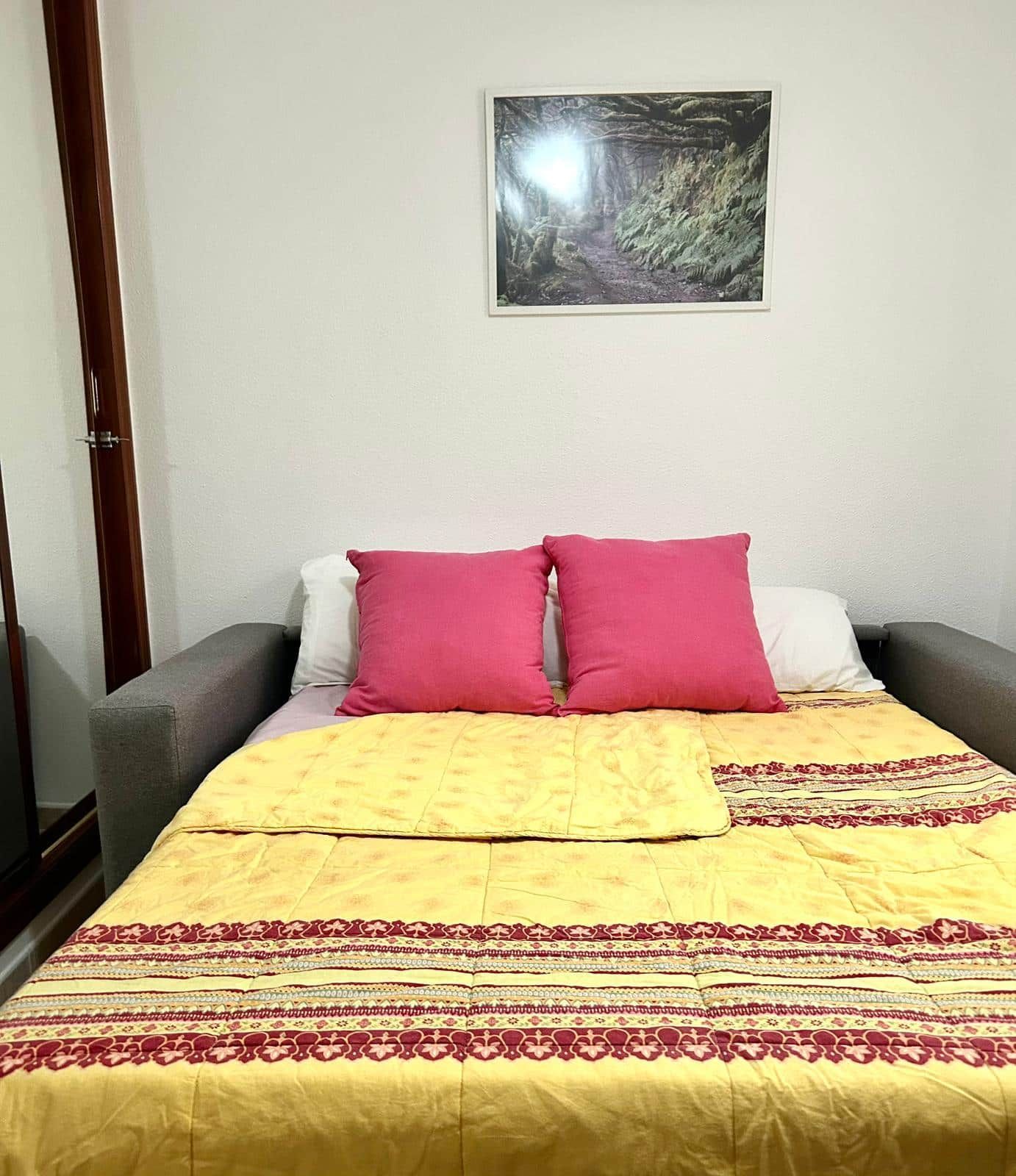 Una cama con un edredón amarillo, almohadas rosas y un cuadro enmarcado en la pared.