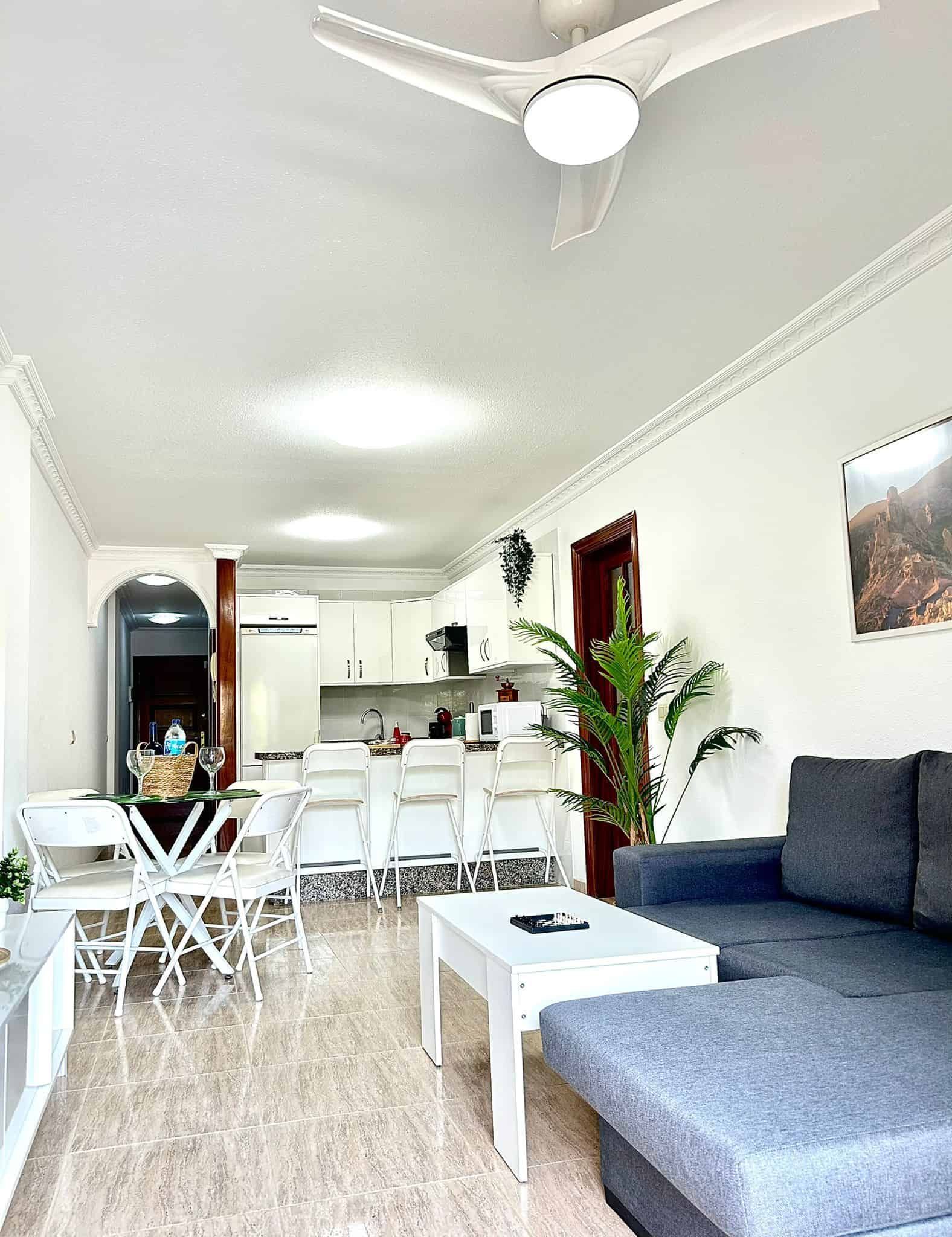 Luminosa sala de estar con diseño abierto, paredes blancas, sofá gris y mesa blanca.