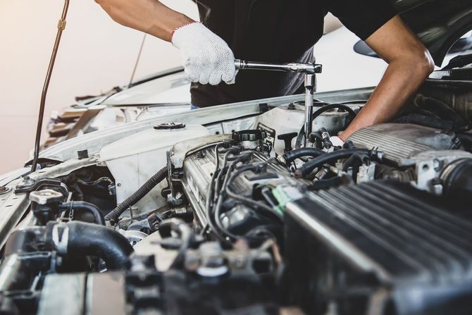Un homme travaille sur le moteur d'une voiture avec une clé.