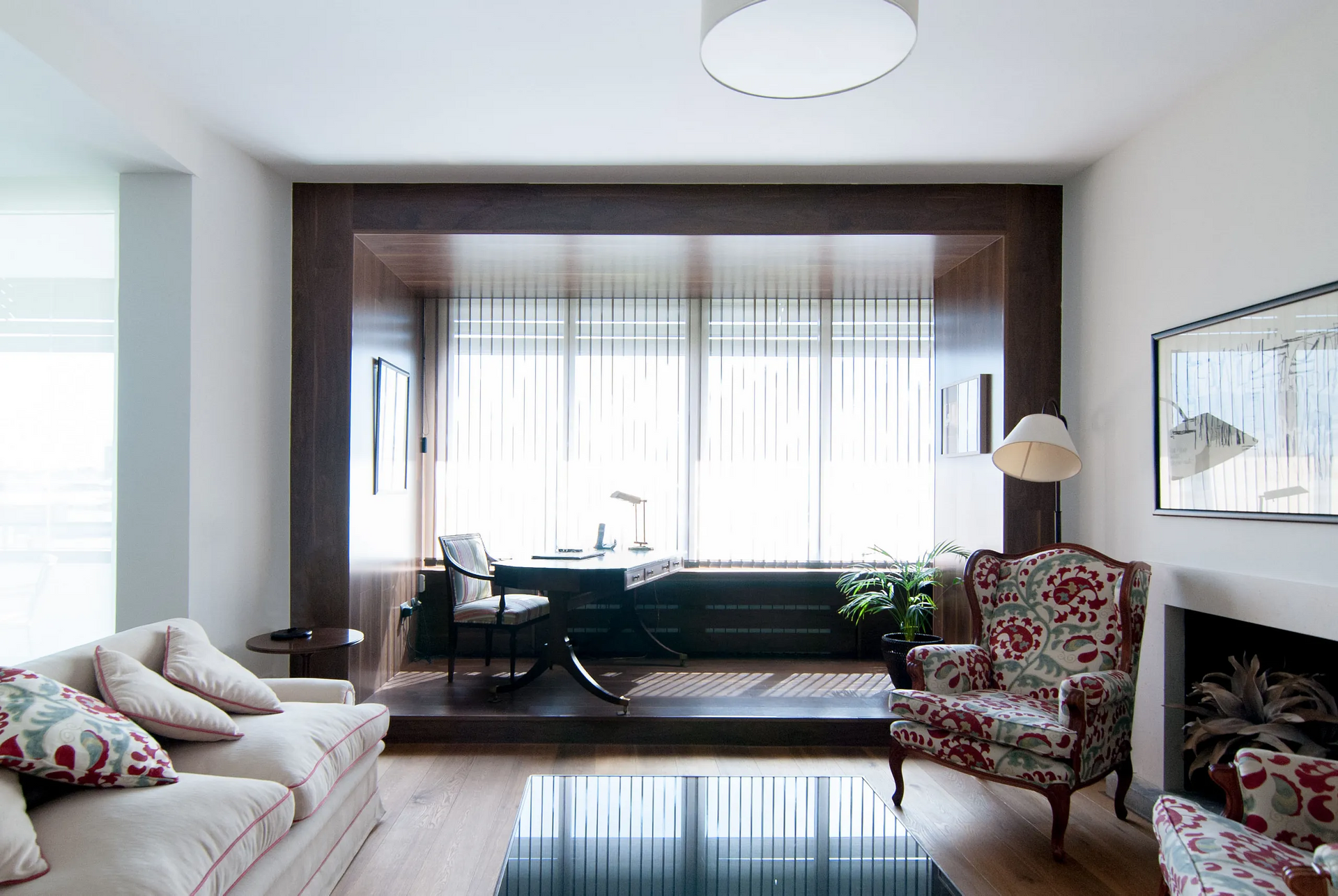 Acogedora sala de estar con sillón floral, sofá, rincón de escritorio y chimenea.