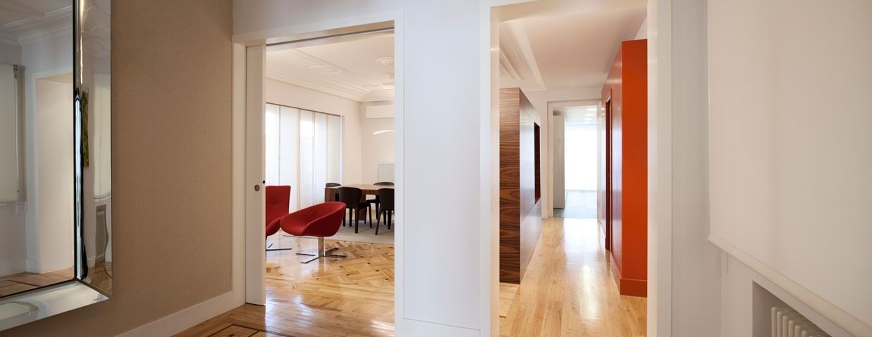 Pasillo con suelo de madera que da paso a un comedor y a un pasillo con pared roja.