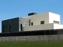 Casa moderna con paredes blancas y negras, césped verde y cielo azul.